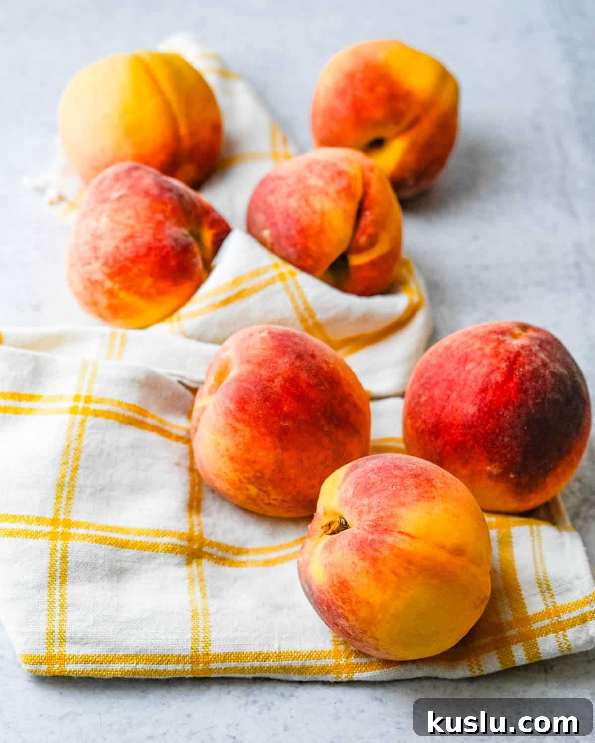 Seven fresh peaches on a dish towel.