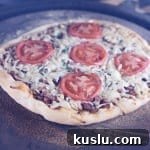 Smoky Brisket Pizza Recipe: How to Make Tender Brisket Pizza at Home 3 Brisket pizza topped with tomato slices on a pizza stone - grilling