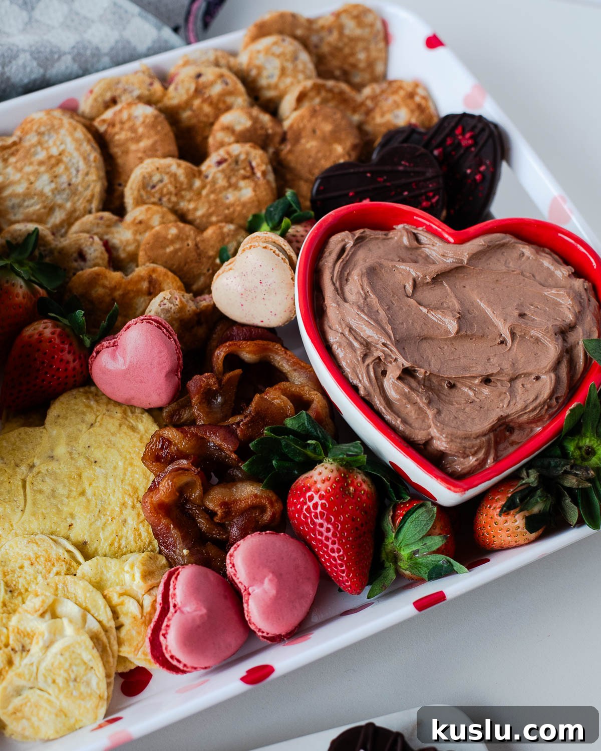 Angled view of a Valentine breakfast board with heart-shaped pancakes, fresh strawberries, heart eggs, bacon, and chocolate yogurt dip.