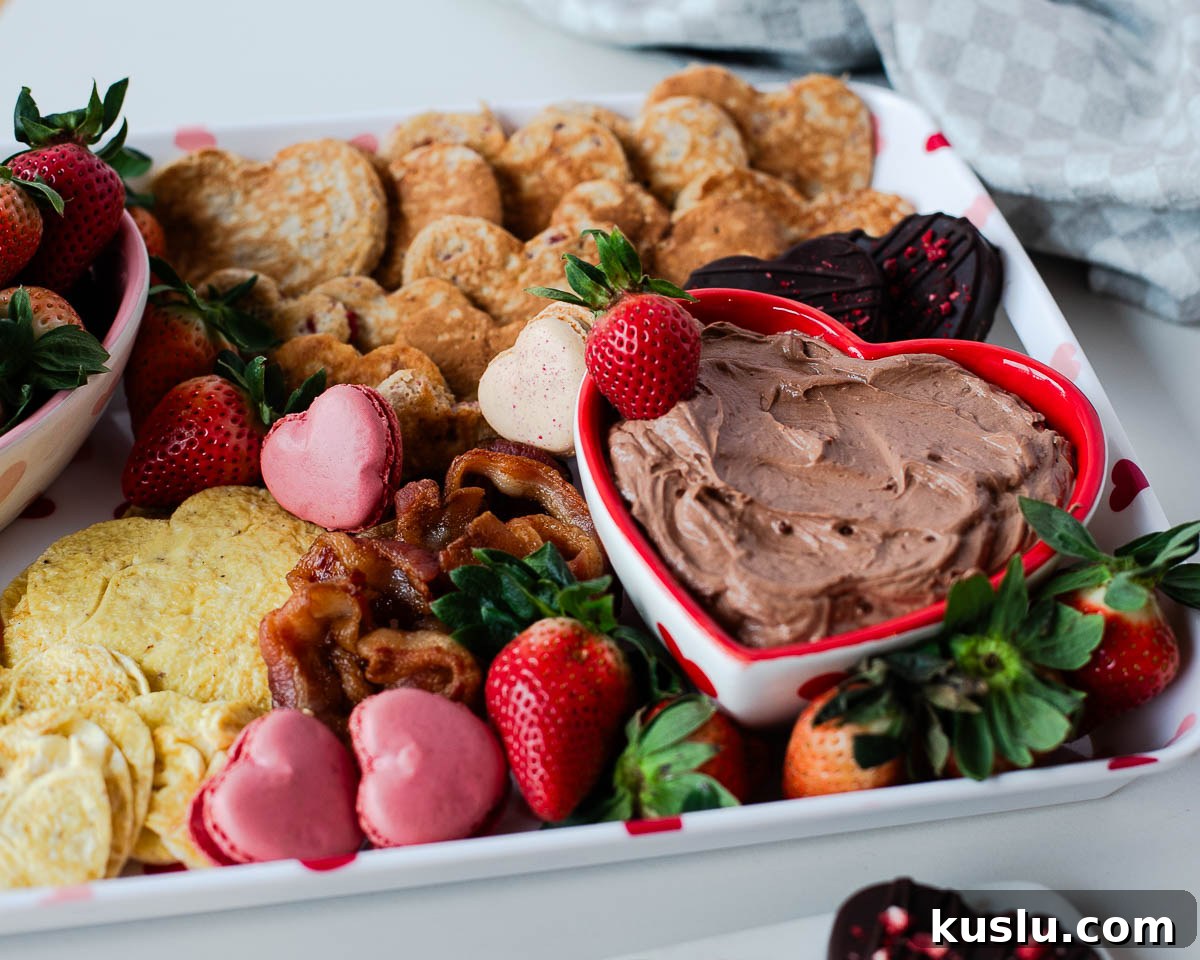 Wide shot of a Valentine breakfast board filled with heart-shaped pancakes, eggs, bacon, strawberries, macarons, and chocolate treats.