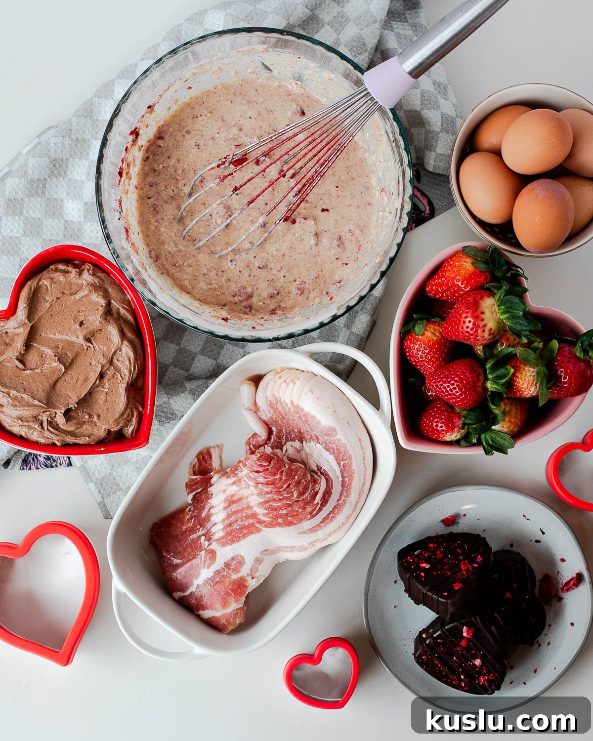Overhead view of Valentine breakfast board ingredients including eggs, strawberries, heart-shaped bacon, protein pancake batter, and chocolate yogurt dip.