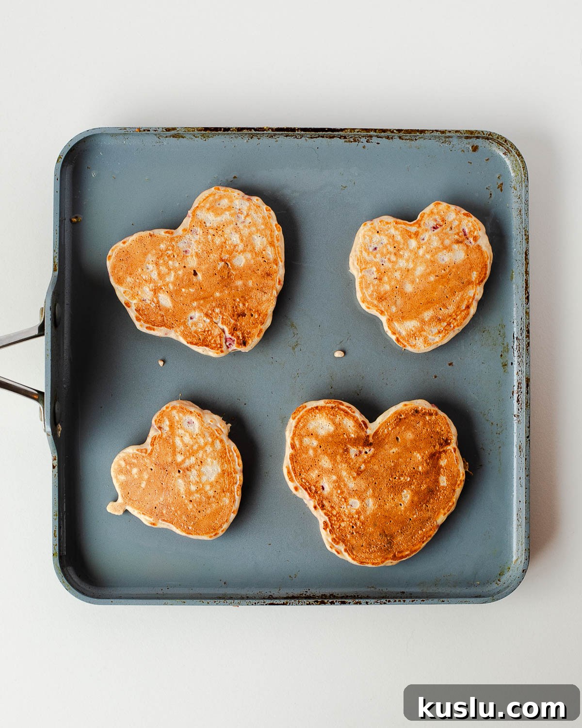 Heart-shaped protein pancakes cooking on a flat griddle for a Valentine breakfast board.