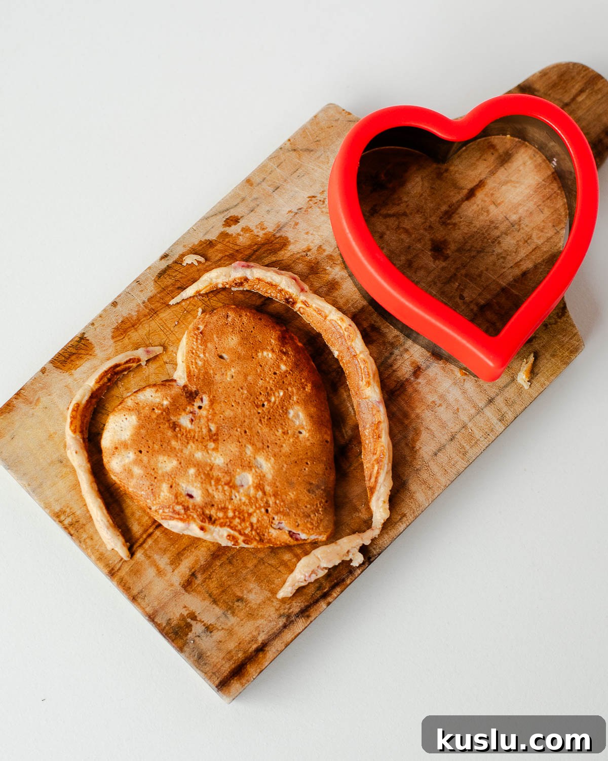 Heart-shaped protein pancake on a wooden cutting board with a red heart-shaped cookie cutter.