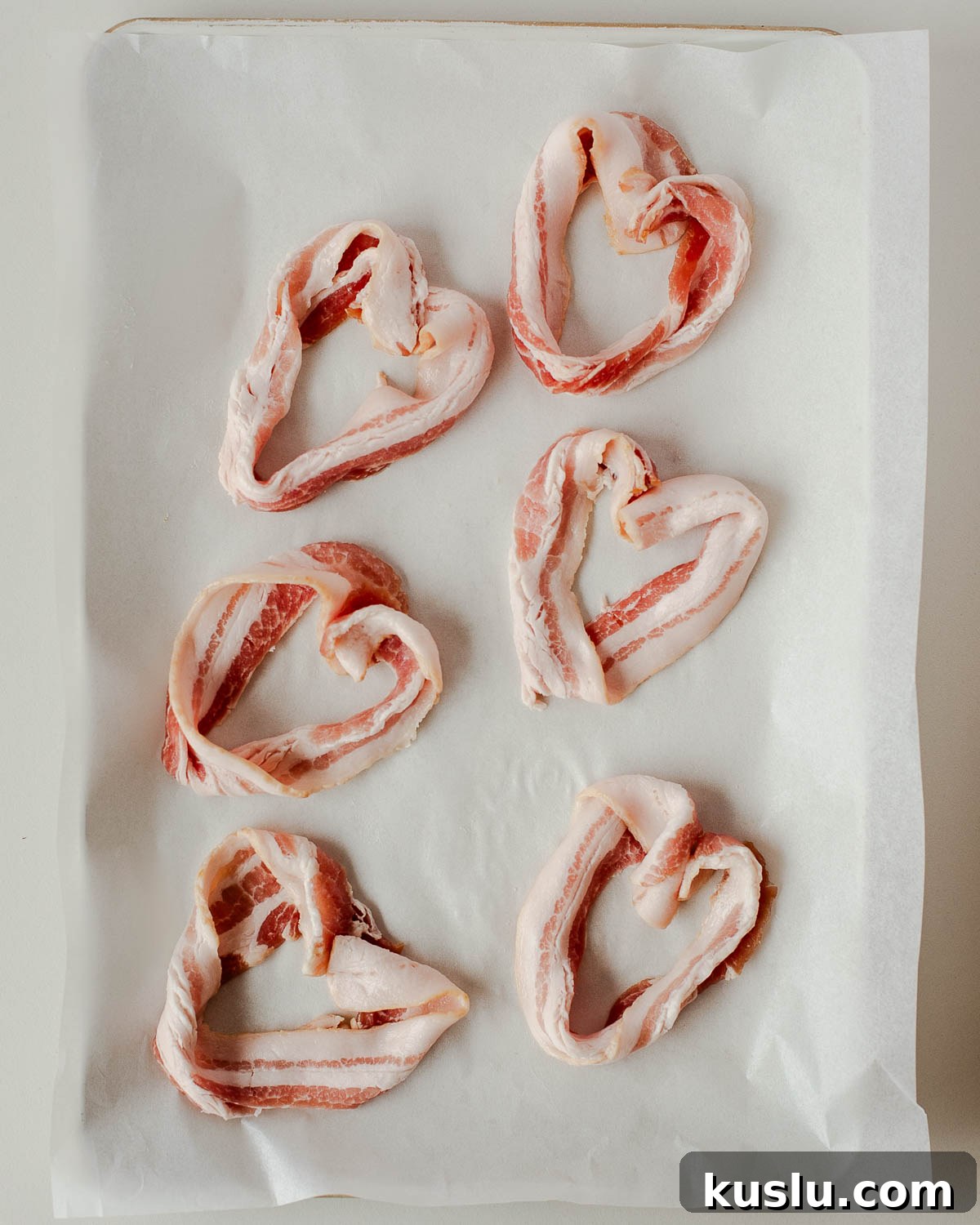 Heart-shaped bacon strips arranged on parchment paper before baking for a Valentine’s Day breakfast board.