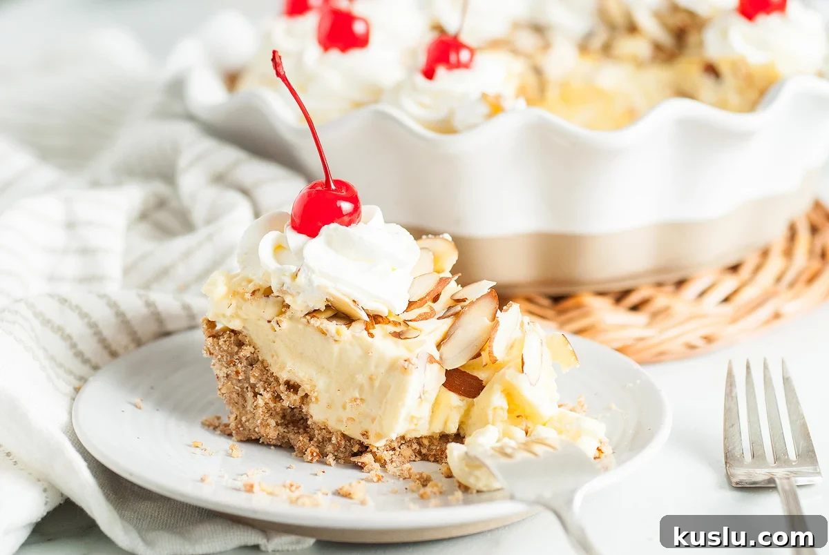 Decadent Amaretto Cream Pie Recipe with Almond Liqueur Filling 2 A slice of Almond amaretto pie with whipped cream, sliced almonds, and a cherry on top, served on a plate with a fork.