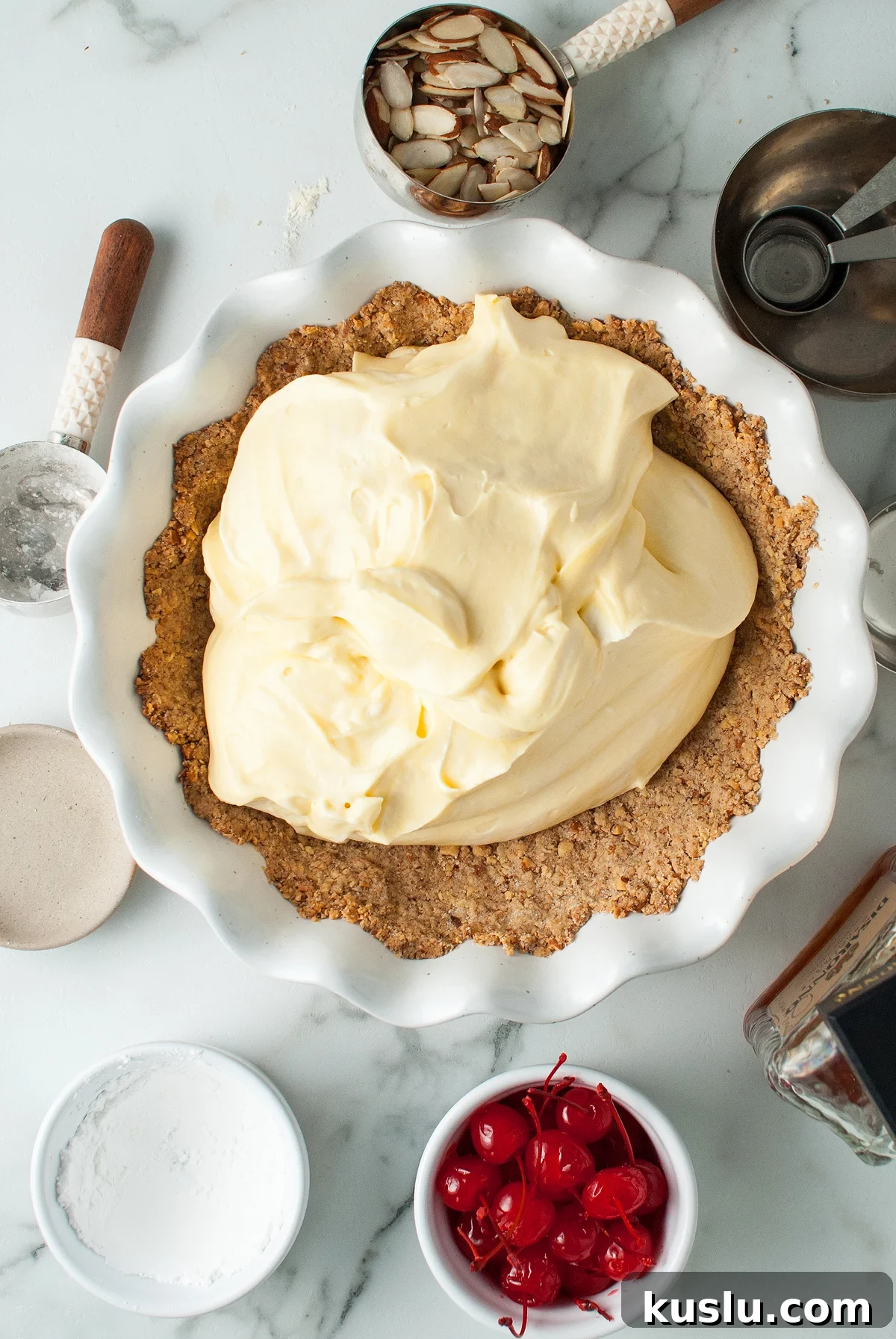 Decadent Amaretto Cream Pie Recipe with Almond Liqueur Filling 17 Overhead view of an almond crust filled with creamy yellow filling, surrounded by baking tools and ingredients—an Italian inspired dessert ready for baking.
