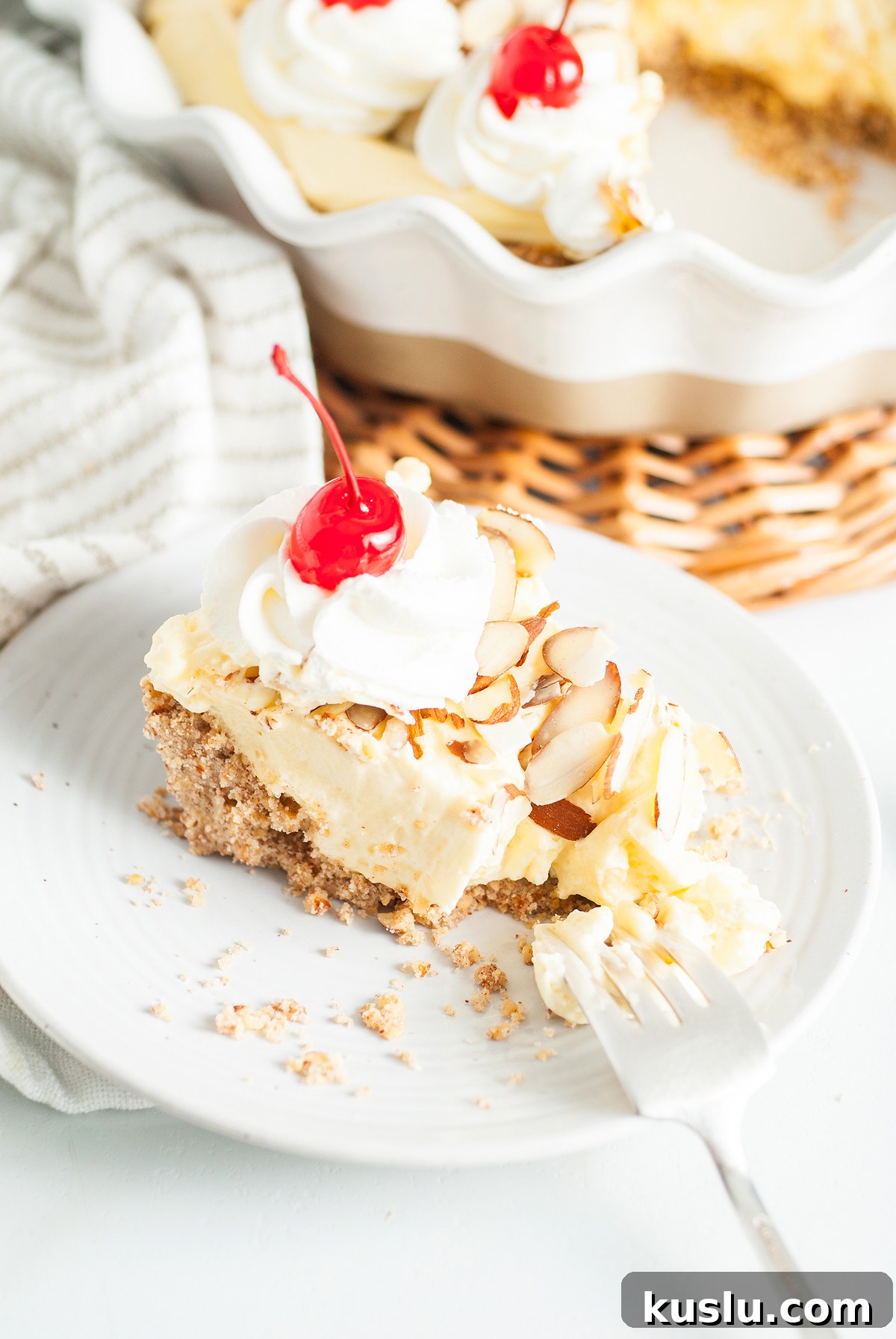Decadent Amaretto Cream Pie Recipe with Almond Liqueur Filling 4 A slice of creamy Almond amaretto pie topped with whipped cream, almond slices, and a cherry sits on a white plate with a fork—an Italian inspired dessert to savor.