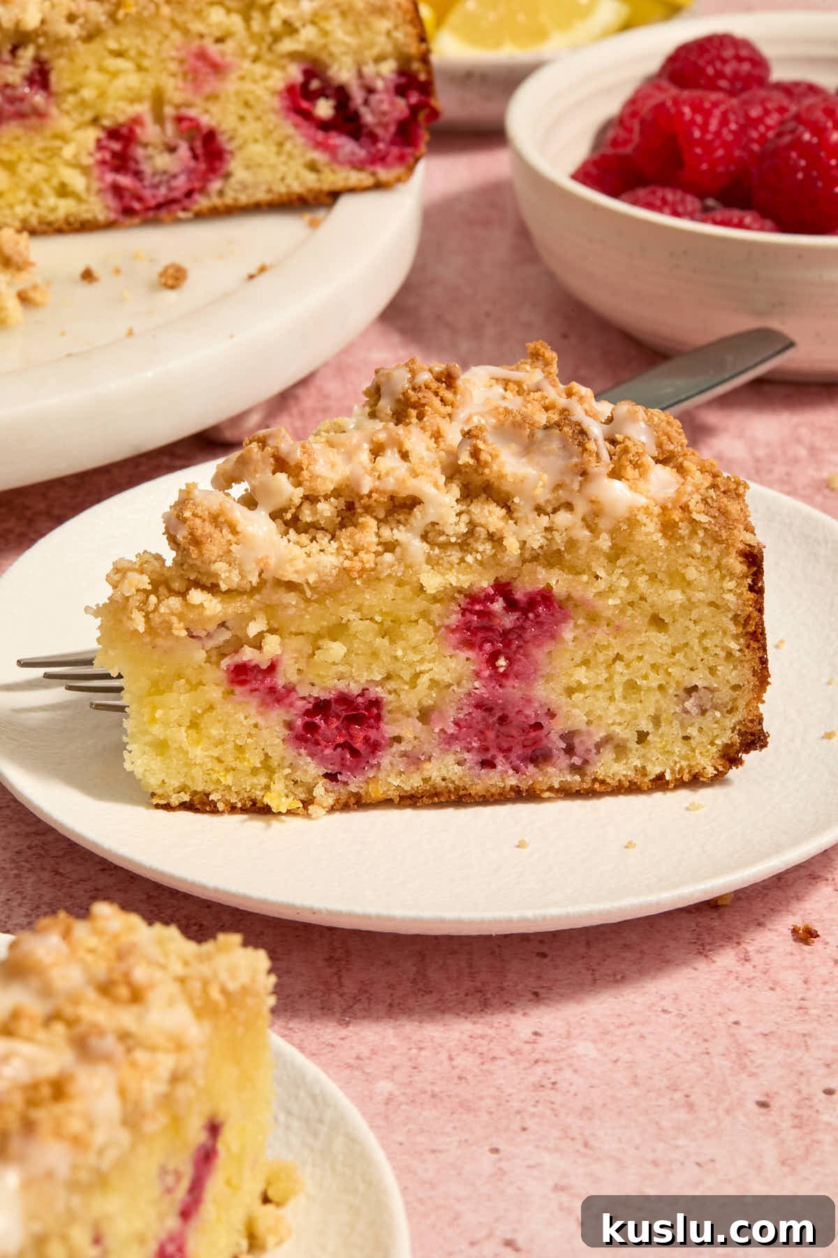 Side view of a slice of raspberry lemon cake on a white plate with a fork.