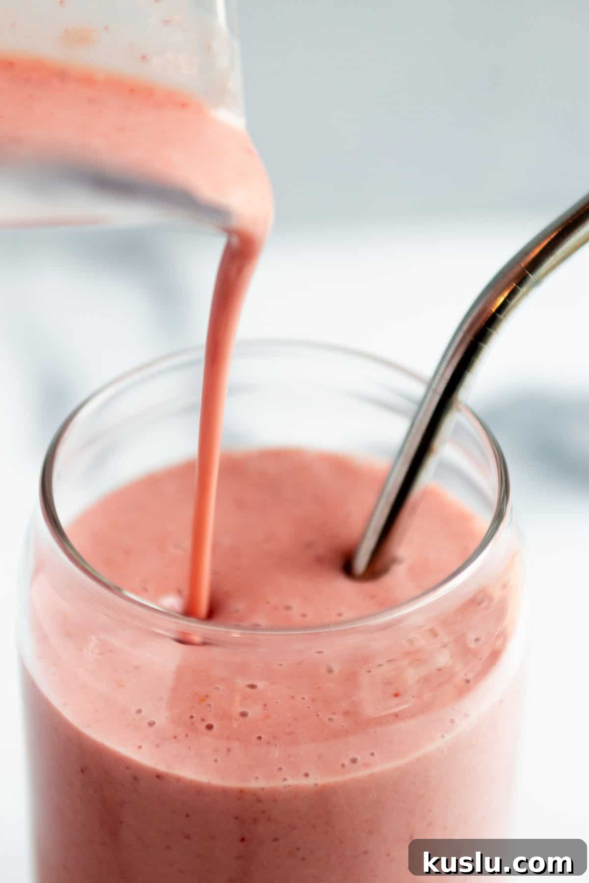 A glass with a banana strawberry smoothie being poured into it.