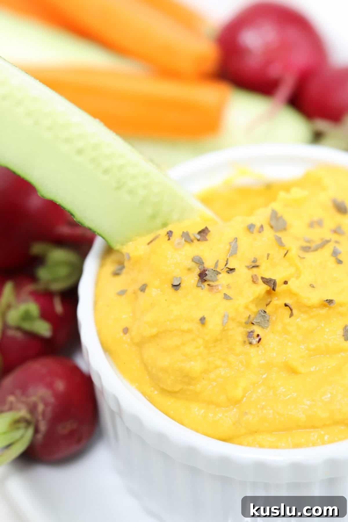 Quick 5-Minute Carrot Hummus Recipe for Busy Weeknights 2 A cucumber spear being dipped into carrot hummus.