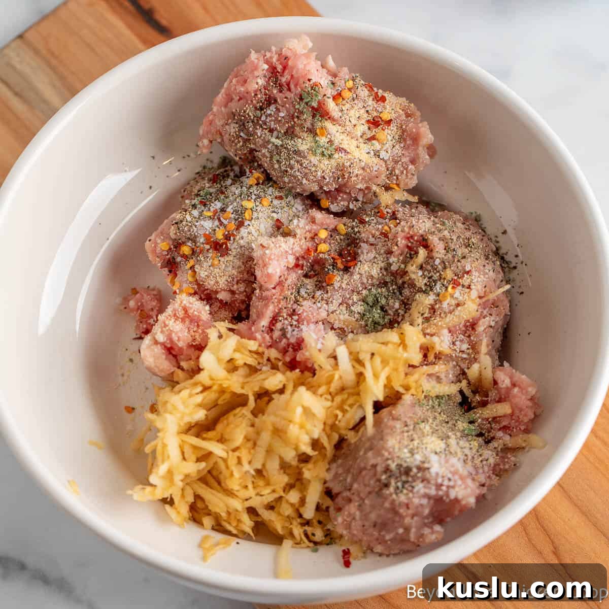 Ground pork, grated apples, and seasoning in a white bowl.