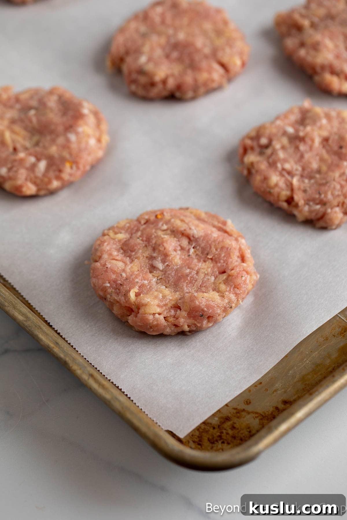 Sausage patties on a baking sheet lined with parchment paper.
