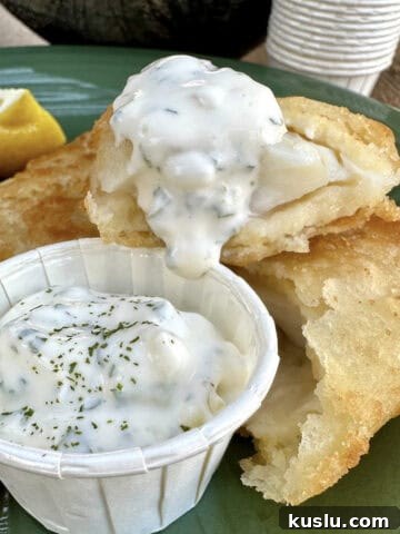 Tartar sauce in a small cup and fried fish on a plate.