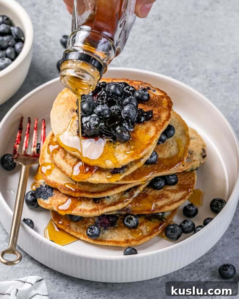 Lemon Blueberry Ricotta Pancakes Recipe for Fluffy, Tangy Stacks 2 maple syrup being added over blueberry pancakes on a plate