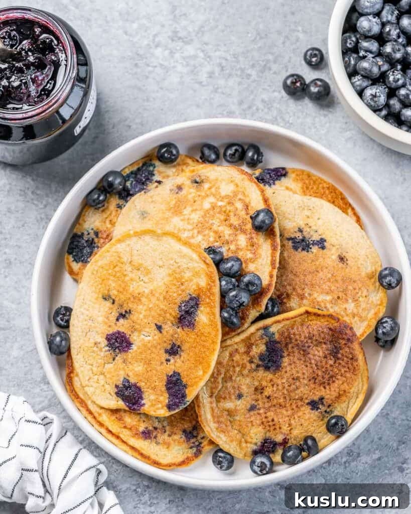 Lemon Blueberry Ricotta Pancakes Recipe for Fluffy, Tangy Stacks 7 Top view of a round deep plate with blueberry pancakes and fresh blueberries over the pancakes.