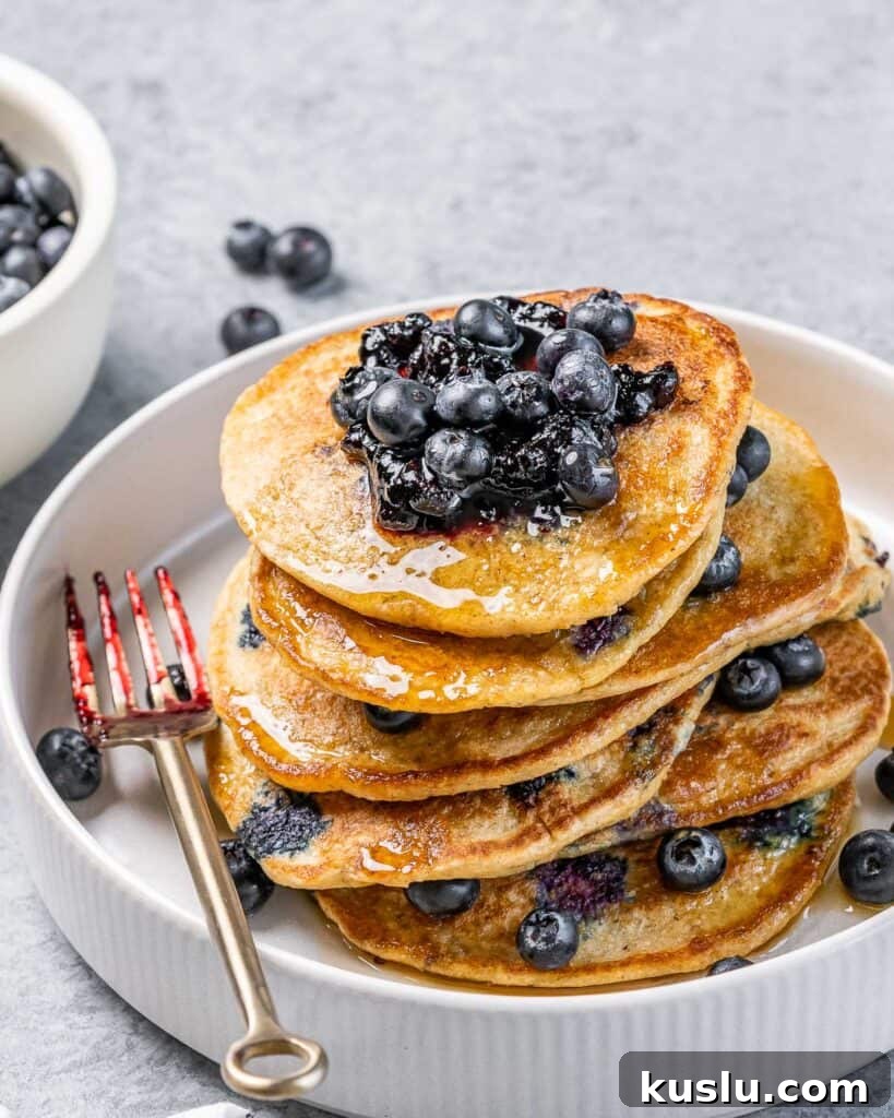 Lemon Blueberry Ricotta Pancakes Recipe for Fluffy, Tangy Stacks 9 Stack of lemon blueberry ricotta pancakes on a white plate with a fork.