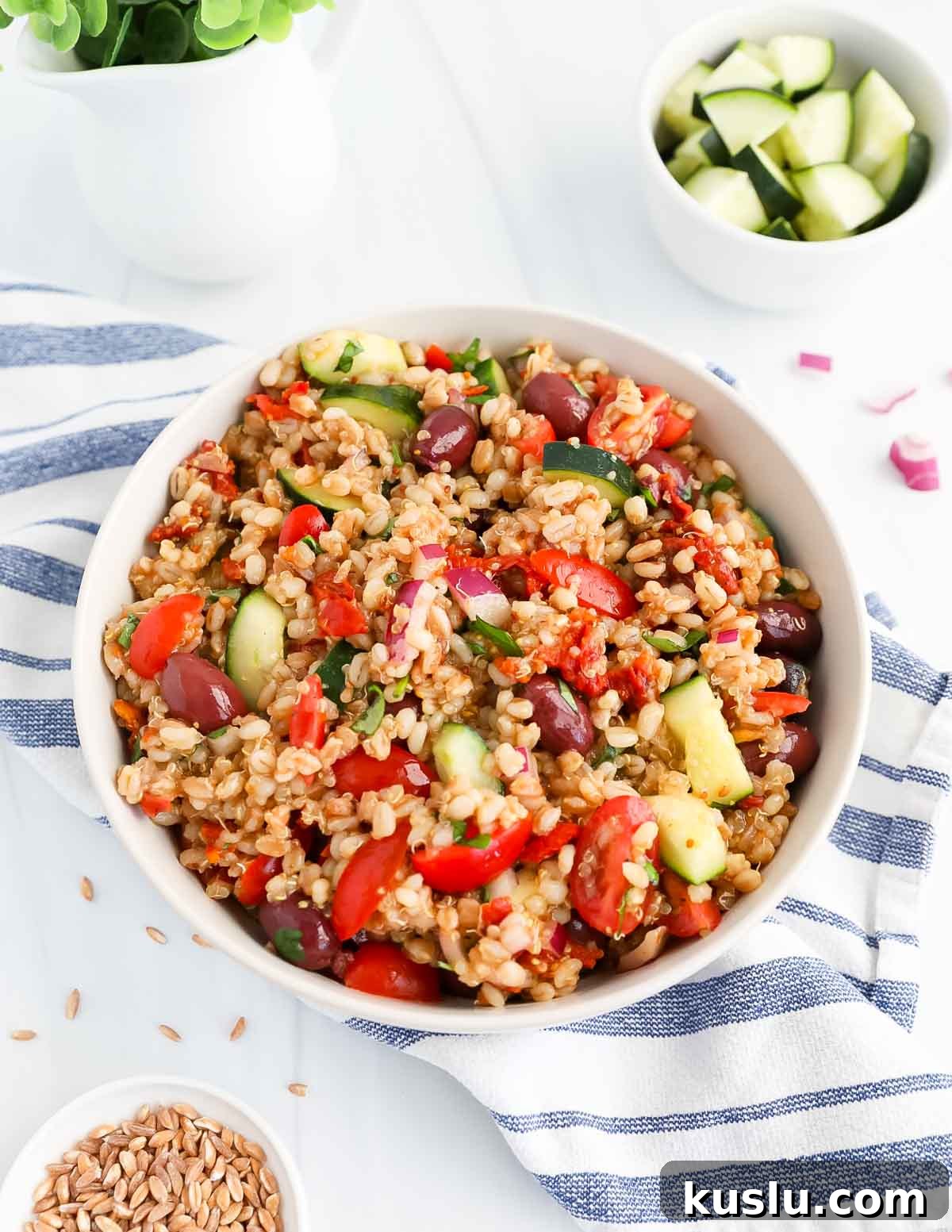 A white bowl filled with grains, vegetables, and kalamata olives.