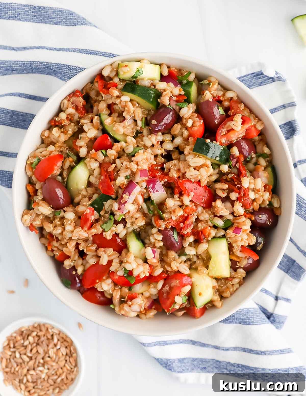 An overhead picture of cooked grain salad with fresh vegetables inside.