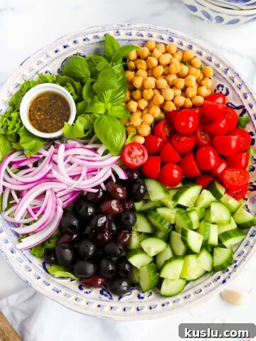 A large salad with lettuce, basil, chickpeas, tomatoes, cucumbers, olives, red onion