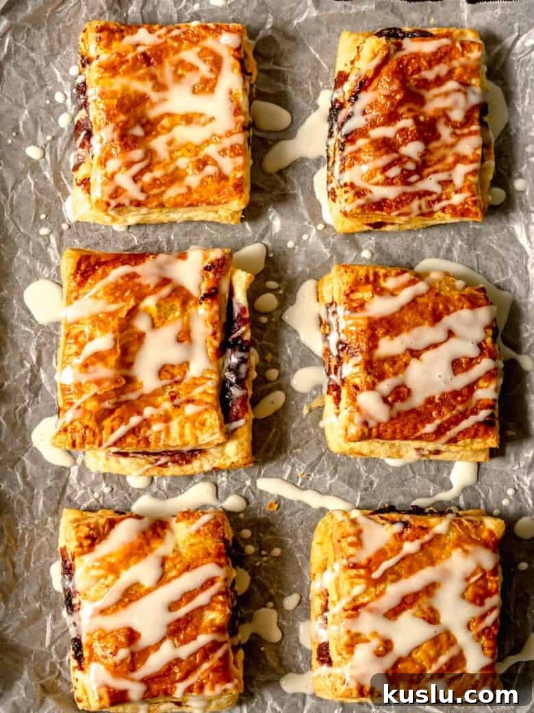 Air Fryer Berry Toaster Strudels: Quick Homemade Breakfast Pastries 2 Glazed air fryer toaster strudels lined up on parchment paper.