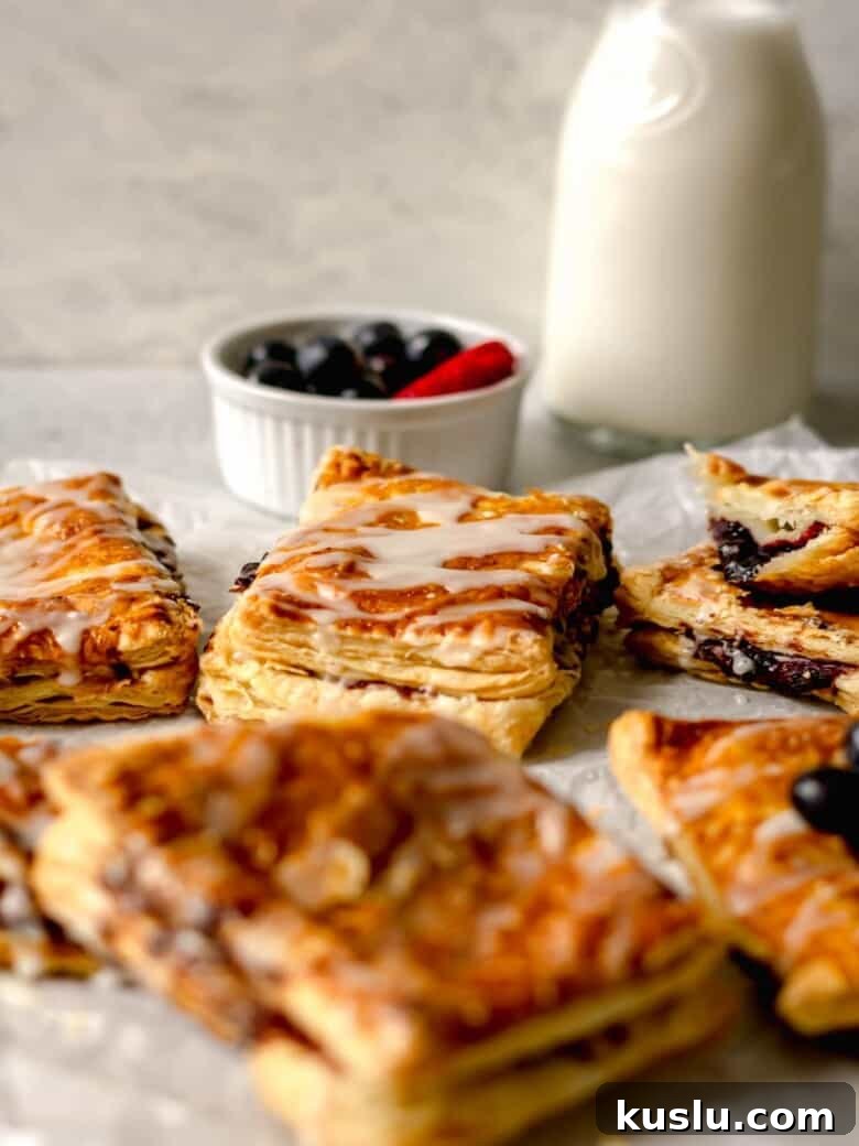 Air Fryer Berry Toaster Strudels: Quick Homemade Breakfast Pastries 6 Puff pastries filled with a berry jam on white parchment paper.
