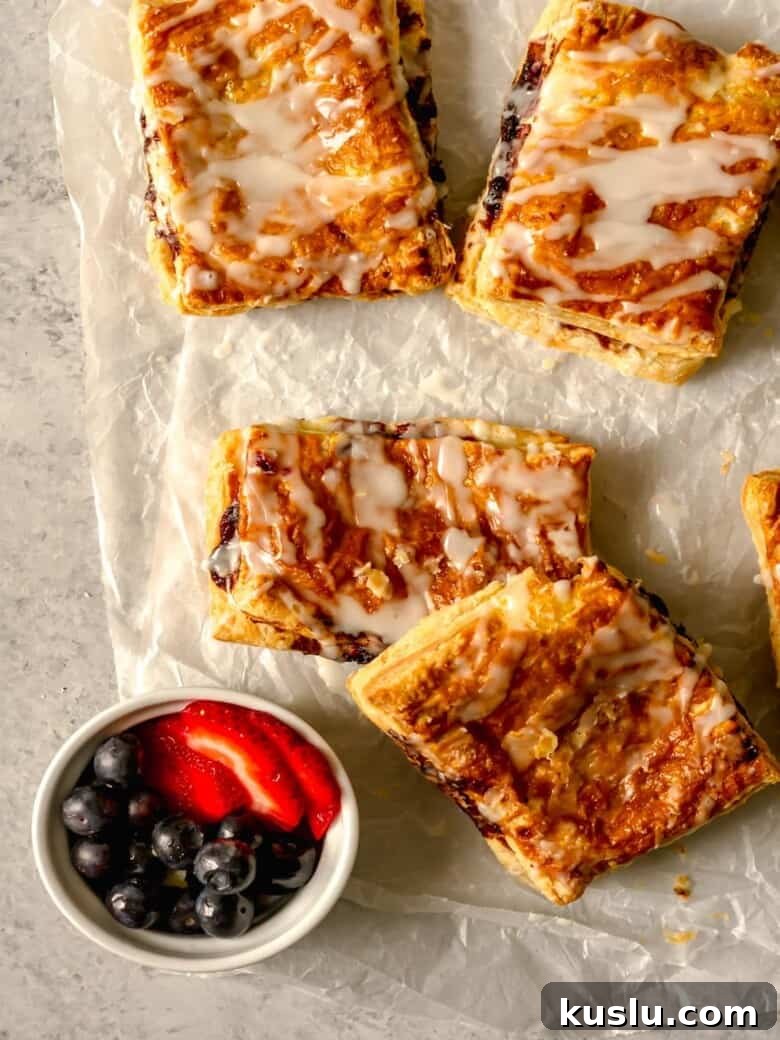 Air Fryer Berry Toaster Strudels: Quick Homemade Breakfast Pastries 7 Glazed puff pastries on white parchment paper.