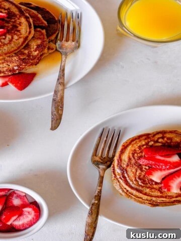 two white plates filled with pancakes and topped with sliced strawberries