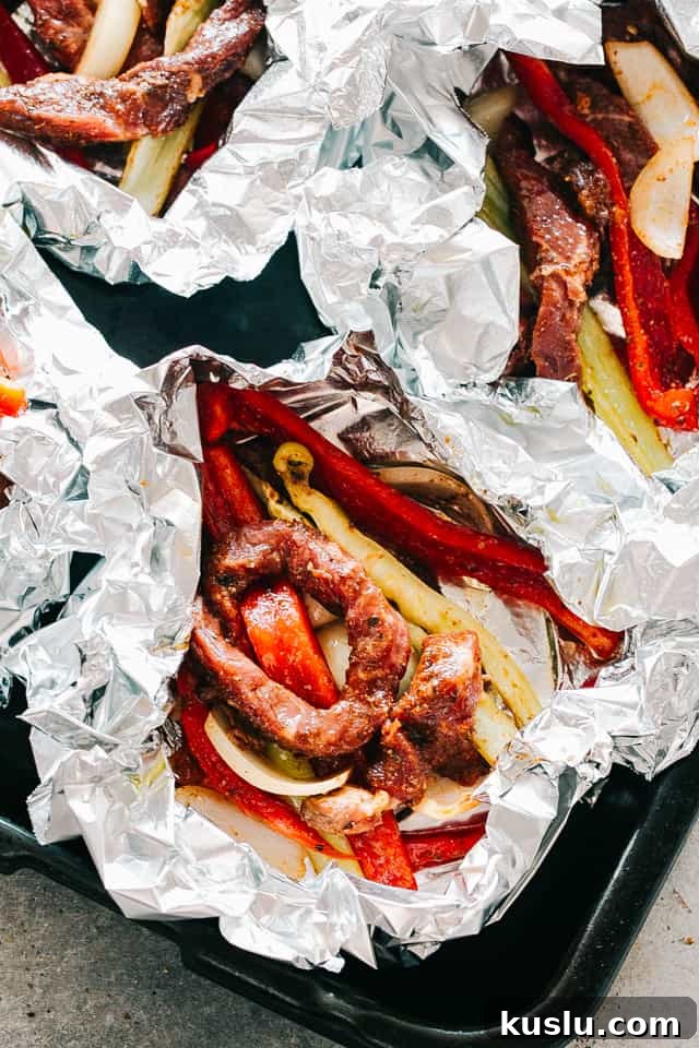 Slices of flank steak, bell peppers, and onions in foil packs.