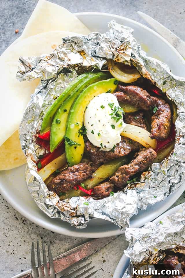 Steak Fajitas in a foil pack, topped with avocado slices and a dollop of sour cream.