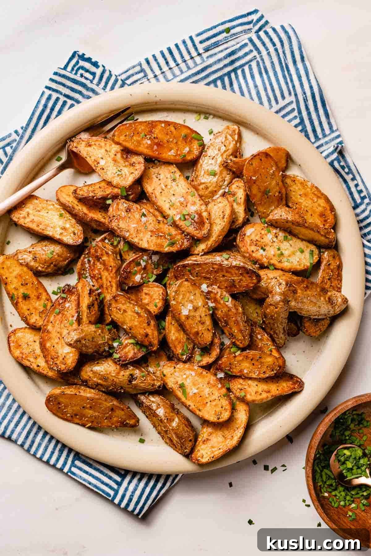 Crispy Air Fryer Fingerling Potatoes Recipe 2 halved fingerling potatoes on plate with herbs on the side