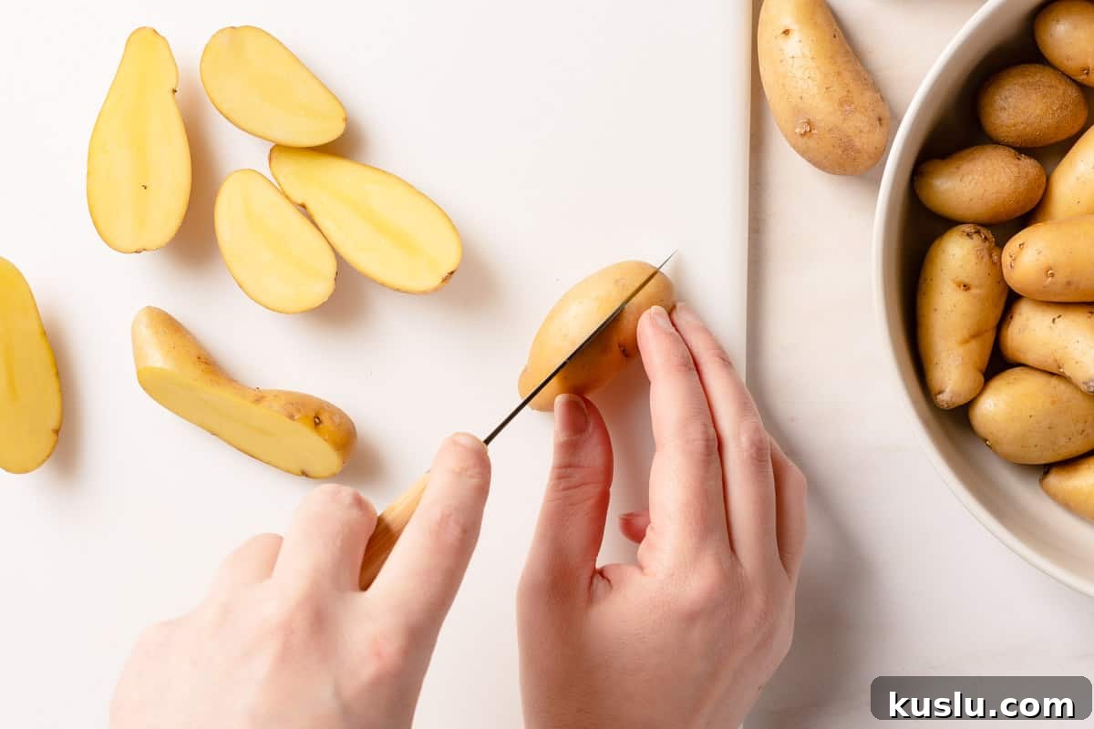 Crispy Air Fryer Fingerling Potatoes Recipe 4 fingerling potato being sliced in half on cutting board with bowl of potatoes on the side