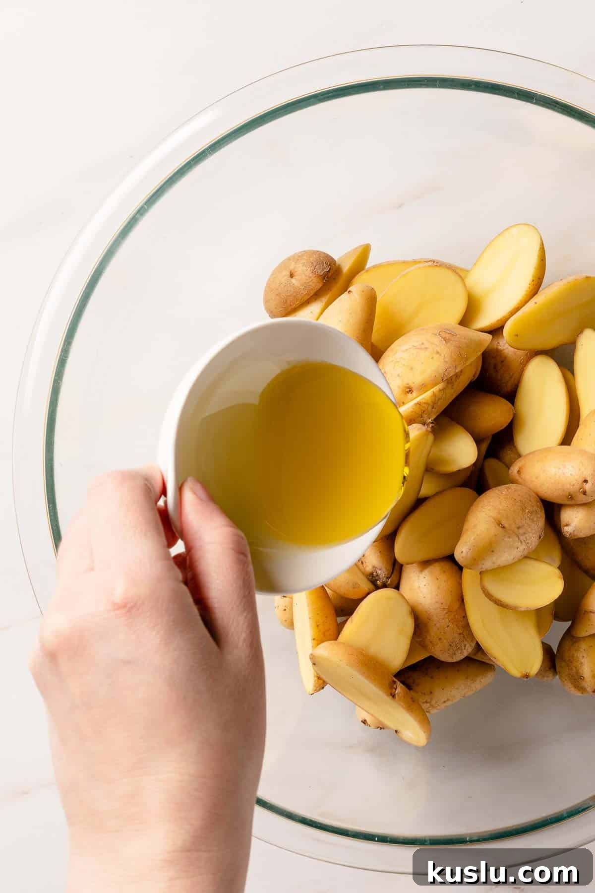 Crispy Air Fryer Fingerling Potatoes Recipe 5 small bowl of oil being poured on top of cut potatoes in bowl