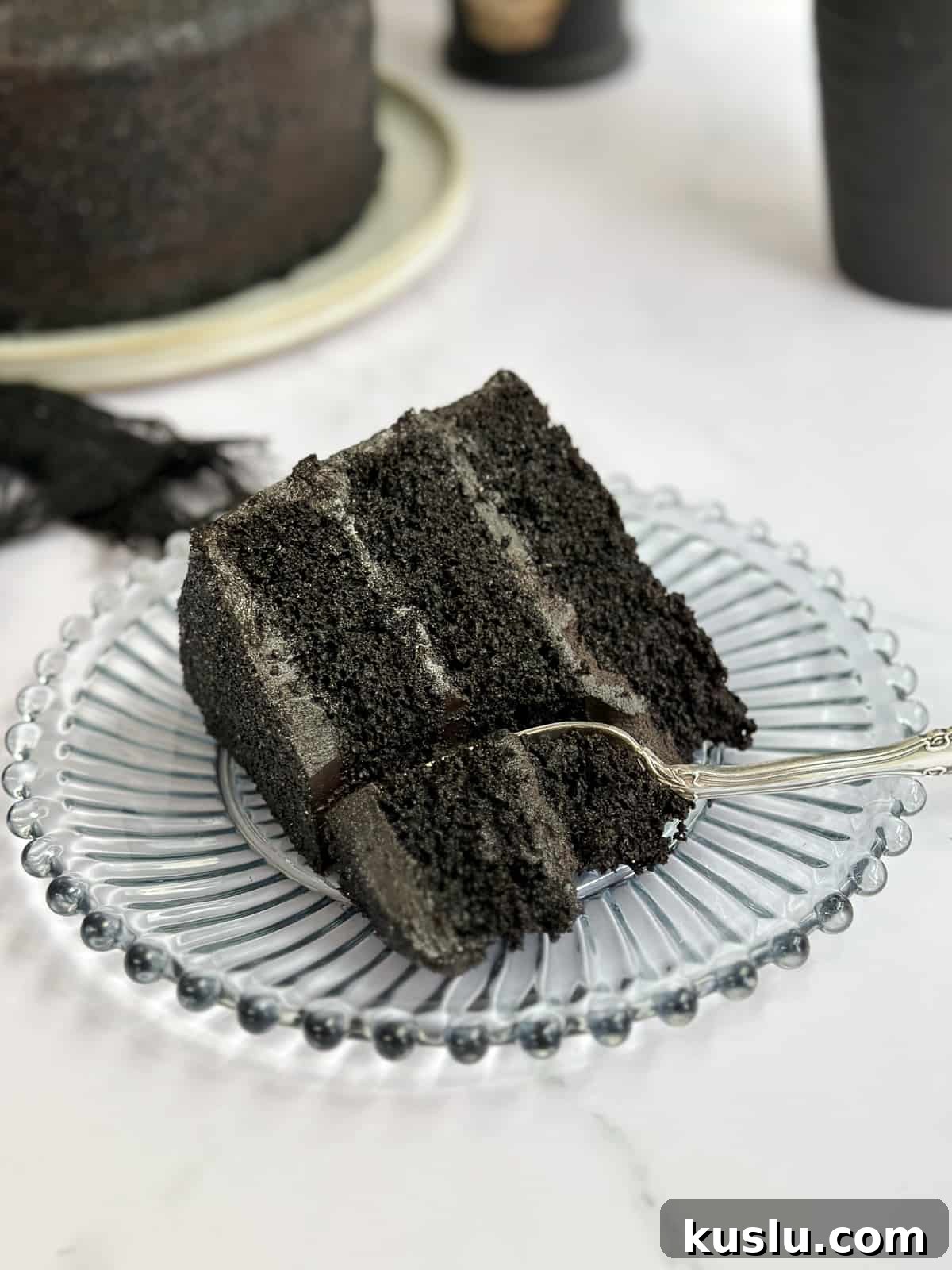 a single slice of black chocolate cake on a plate with a fork cutting though it.