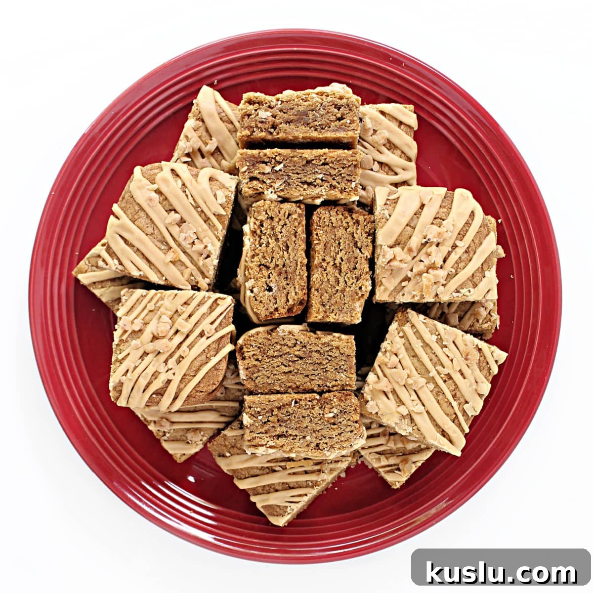 Biscoff Blondie Bars: Chewy Lotus Biscoff Cookie Dessert 7 A serving plate filled with Biscoff Blondie bars topped with drizzled Biscoff icing and sprinkled with crunchy toffee bits.