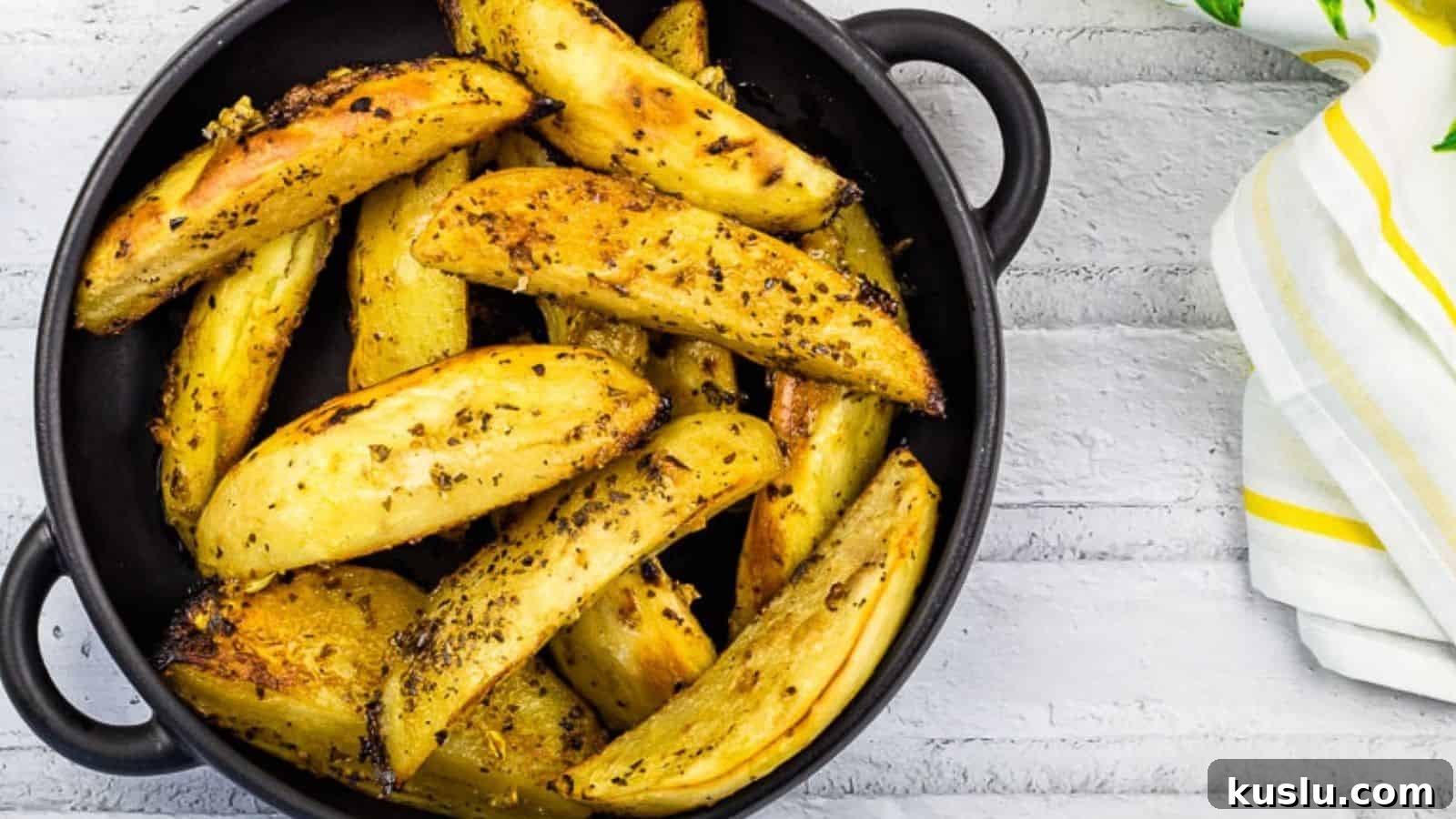 17 Tangy Lemon Recipes Made for Flavor, Not Fancy Presentation 14 Round black dish filled with seasoned roasted potato wedges, placed on a white wooden surface alongside a white and yellow striped cloth napkin.
