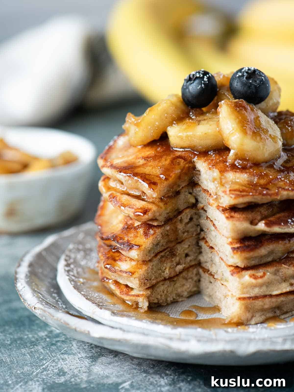 A stack of banana bread pancakes cut open to see inside with bananas on top.