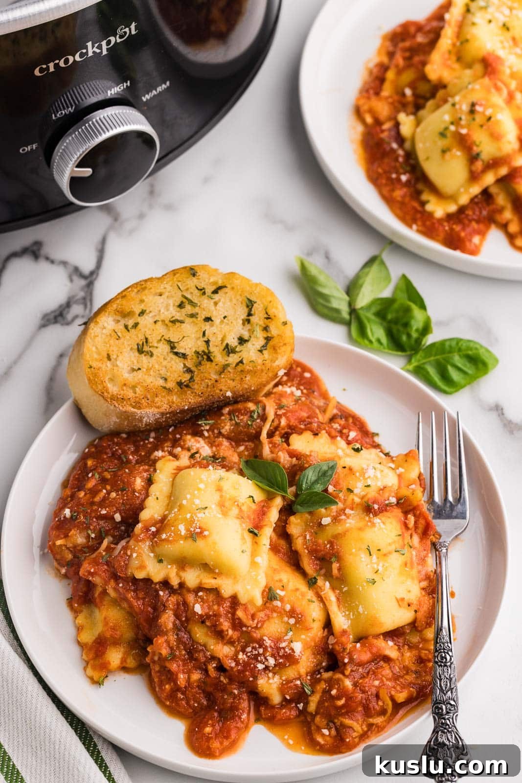 Slow Cooker Ravioli Lasagna: Comforting One-Pot Dinner 2 overhead view of two plates of cooked ravioli lasagna with a fork and garlic bread, with black slow cooker in the background