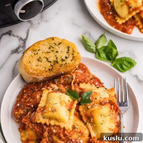 overhead view of two plates of cooked ravioli lasagna with a fork and garlic bread, with black slow cooker in the background