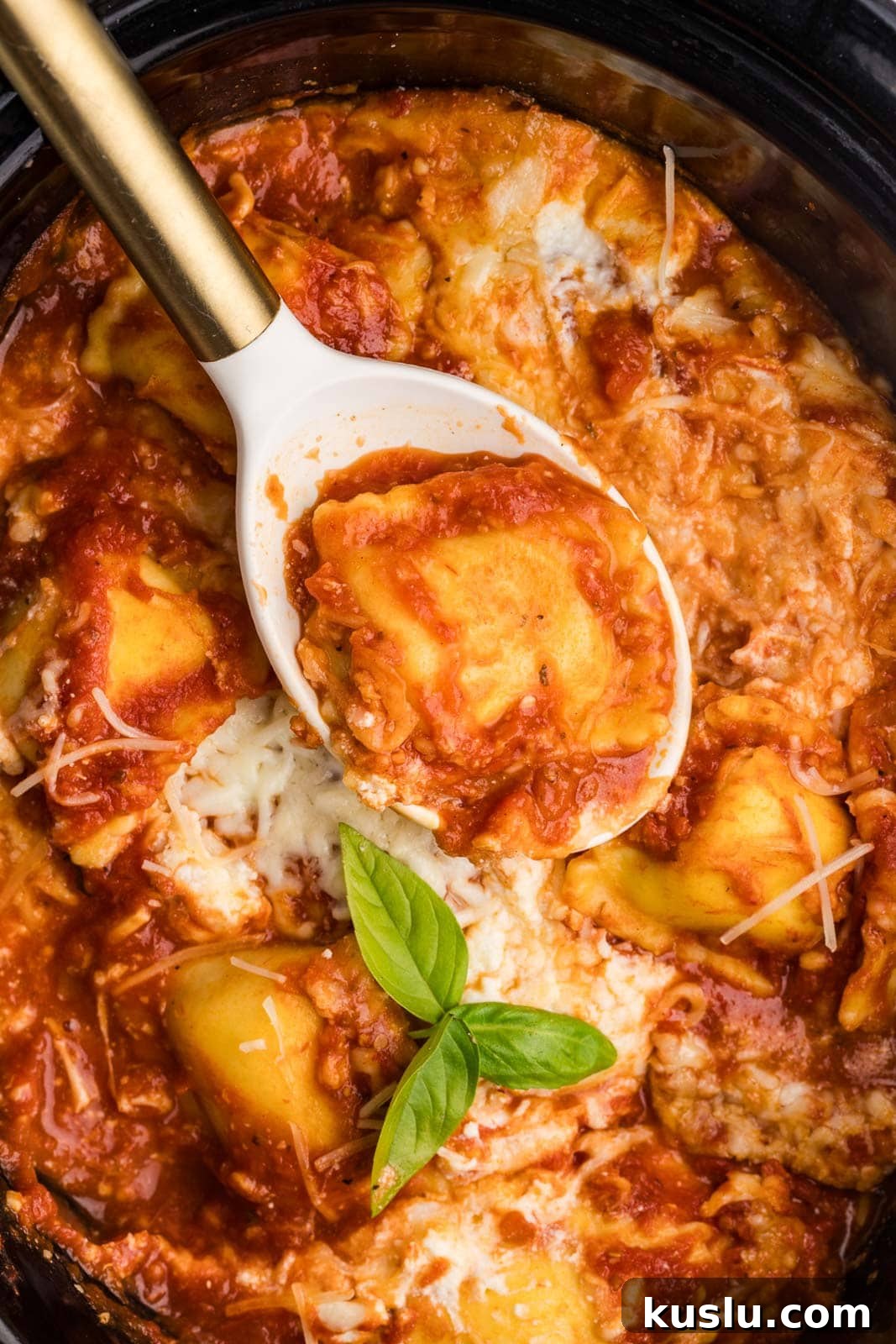 Slow Cooker Ravioli Lasagna: Comforting One-Pot Dinner 5 overhead view of black slow cooker with large white spoon with gold handle containing ravioli with cooked ravioli lasagna in background