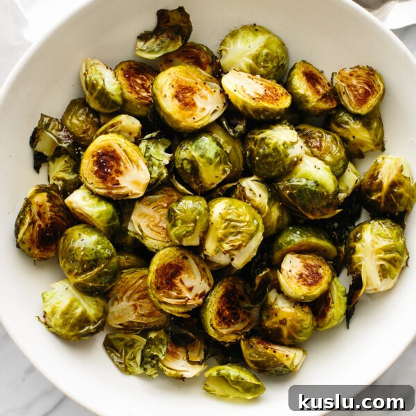 A bowl of roasted Brussels sprouts on a table next to a spoon.