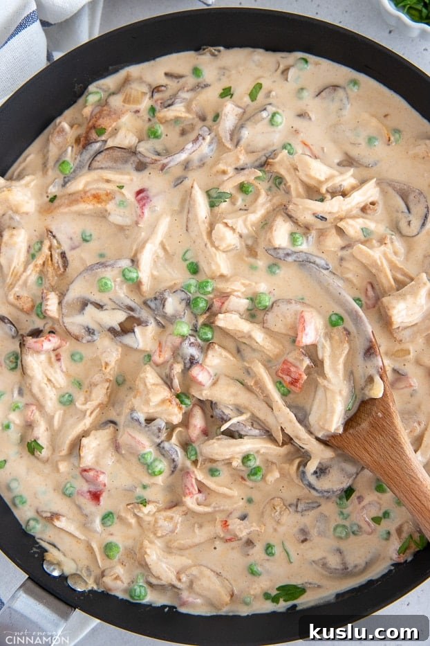 overhead shot of a skillet with creamy dairyfree chicken a la king with a wooden spoon
