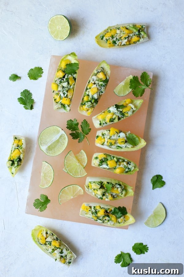 Photo of Crab Mango and Avocado Salad with Chile Lime Dressing in Endive on pink salt block garnished with limes and cilantro.