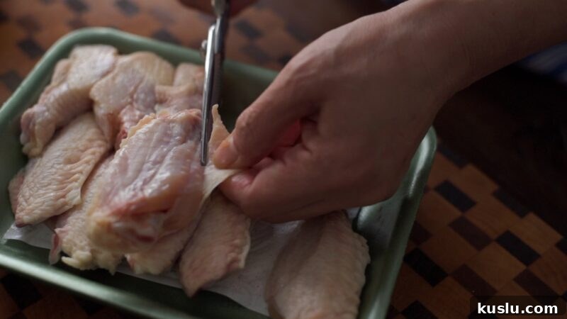 Trimming loose skin from chicken wings with kitchen scissors