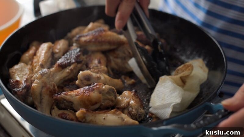 Paper towel blotting excess fat from skillet of chicken wings