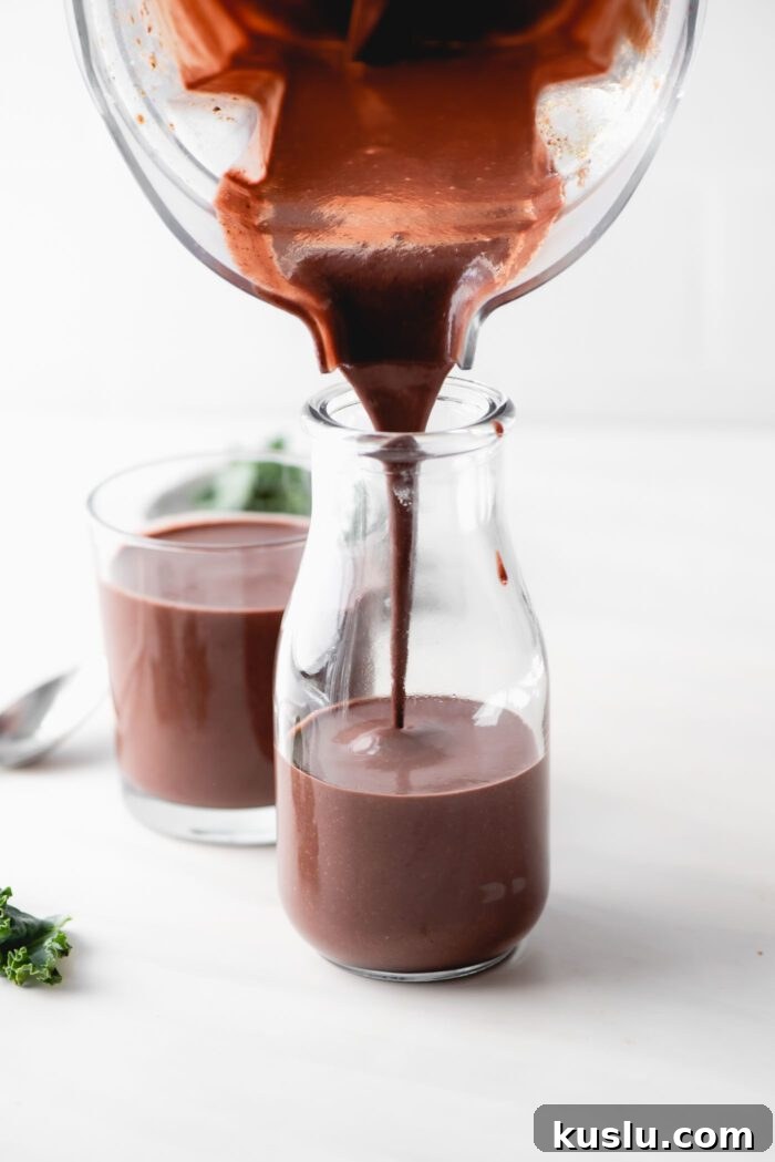 Pouring a chocolate smoothie from a blender into a glass jar.