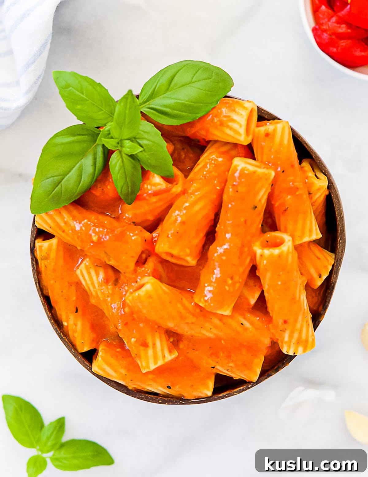 A coconut bowl with rigatoni pasta inside covered with pasta sauce and garnished with fresh basil.