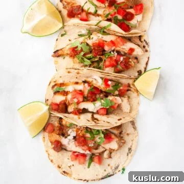 a top down view of a line of grilled chicken tacos surrounded by lime wedges.