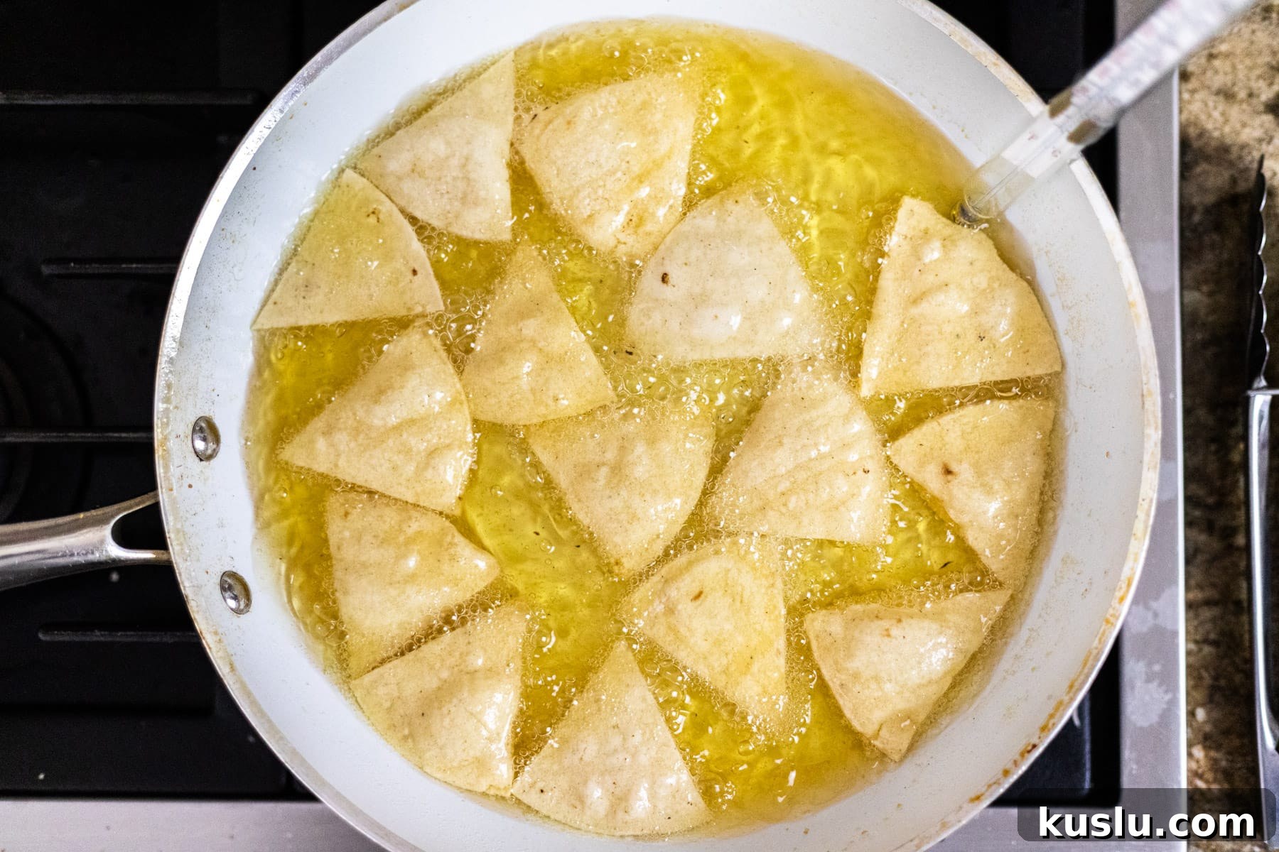Corn tortilla chips frying in oil in a frying pan.