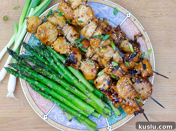 four Grilled Asian Chicken Kabobs on a plate with grilled asparagus