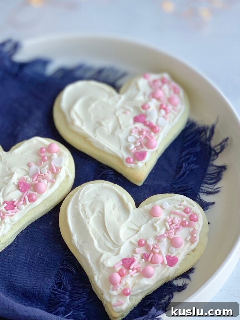 3 heart shaped sugar cookies with white frosting and pink and white sprinkles on the right side of each cookie.